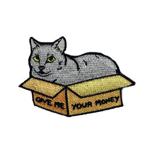 An embroidered patch of a grey cat sitting in a box, which reads "GIVE ME YOUR MONEY".