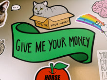 Load image into Gallery viewer, The green banner sticker that says &quot;GIVE ME YOUR MONEY&quot;, surrounded by other stickers.